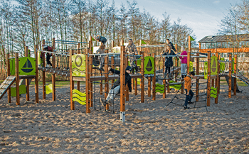 Børn leger og klatrer på en legeplads med et kæmpestort klatretårn og sandunderlag