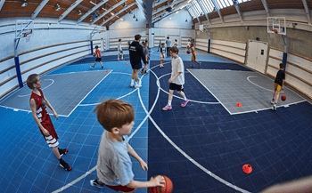 Idrætshal med basketstativer, hvor børnene spiller basketball